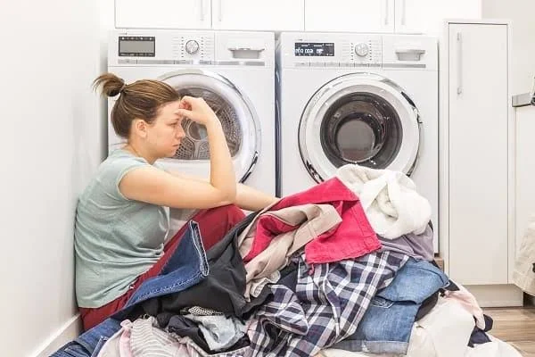Washer not working in Cape Coral, frustrated woman sitting next to a pile of laundry beside a broken washer and dryer